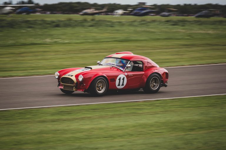 Oliver Bryant driving the red and gold 1965 AC Cobra at Goodwood Revival in 2018