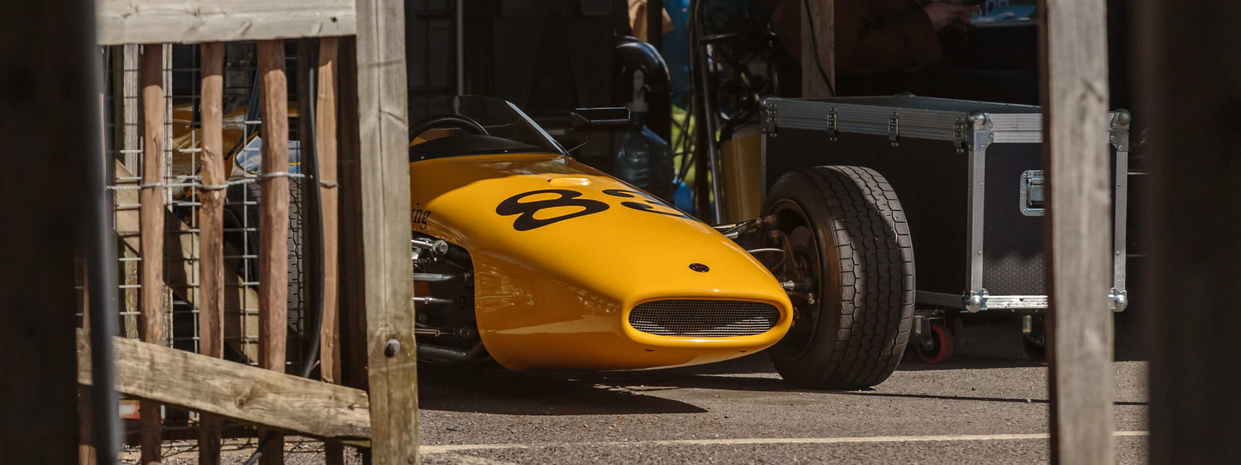 Yellow classic formula one race car sat in the Goodwood paddock.